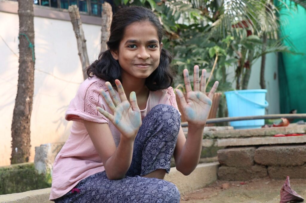 A girl with painted hands waves and smiles